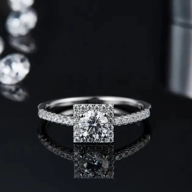 A radiant engagement ring with a 0.50ct moissanite center stone and a halo of shimmering moissanites, set in a polished sterling silver band.