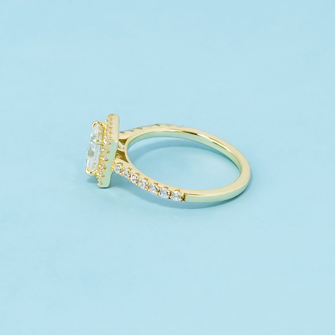A beautiful halo design accentuates the sparkle of a princess cut moissanite in this 9ct yellow gold ring.