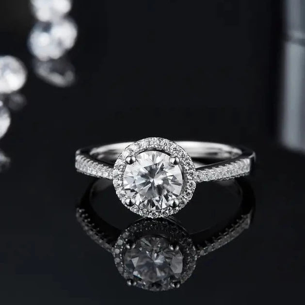 This stunning ring showcases a 1.00ct moissanite surrounded by a halo of sparkling hearts, crafted in 9ct white gold.