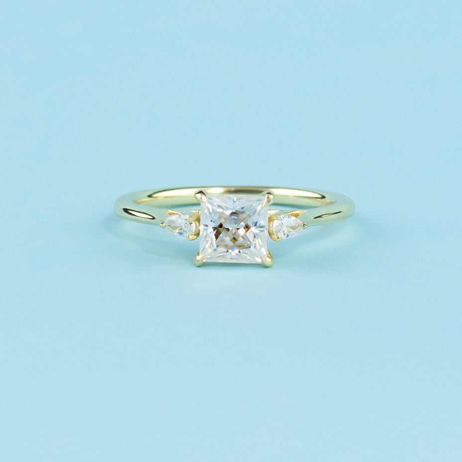 This elegant ring showcases three sparkling princess cut moissanites in a warm 9ct yellow gold setting.