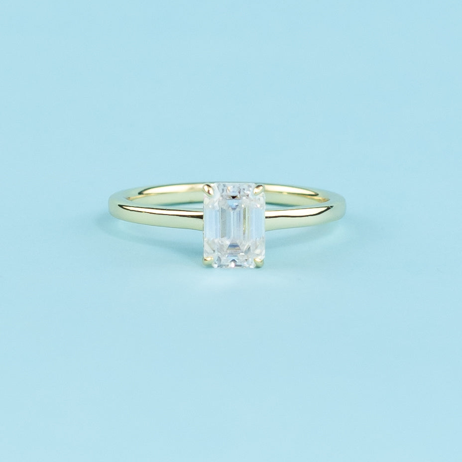 Discover the secret sparkle of this elegant ring with a hidden halo surrounding a brilliant emerald cut moissanite.