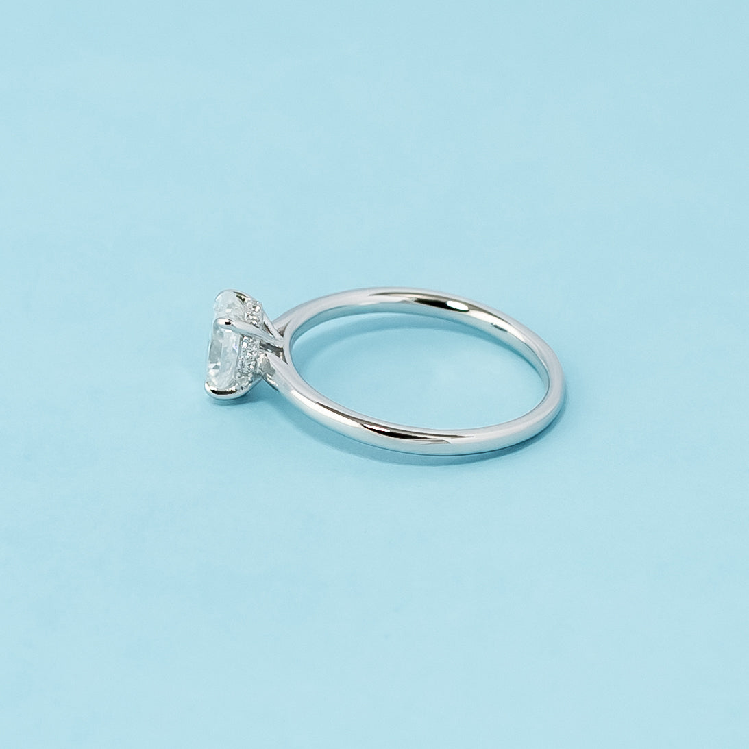 Modern and sophisticated engagement ring showcasing an oval cut moissanite in a unique hidden halo design, crafted in 9ct white gold.