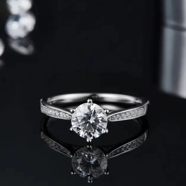 This 1.00ct moissanite engagement ring exudes luxury with its elegant tapered pave setting in 9ct white gold.