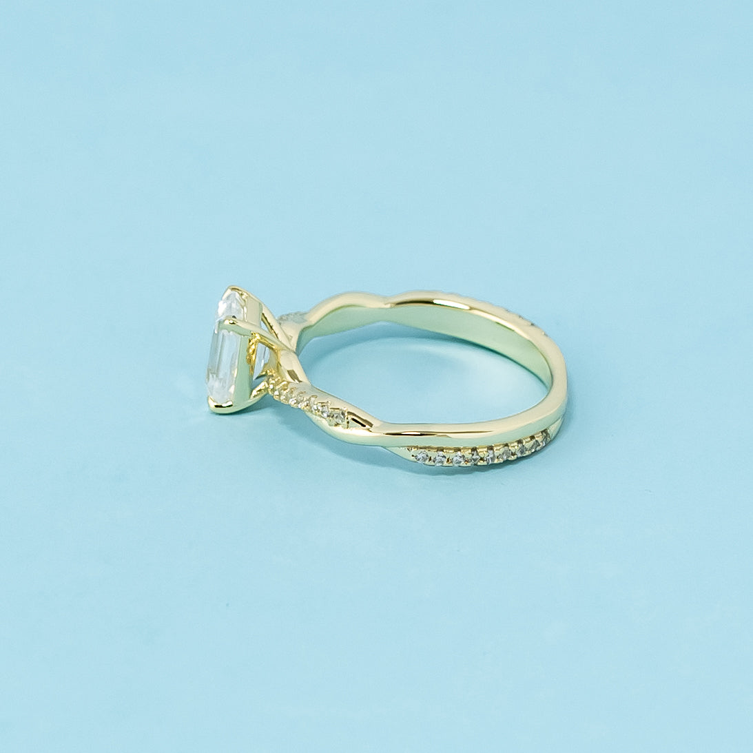 This 9ct yellow gold ring features a classic emerald cut moissanite with a delicate infinity design element.