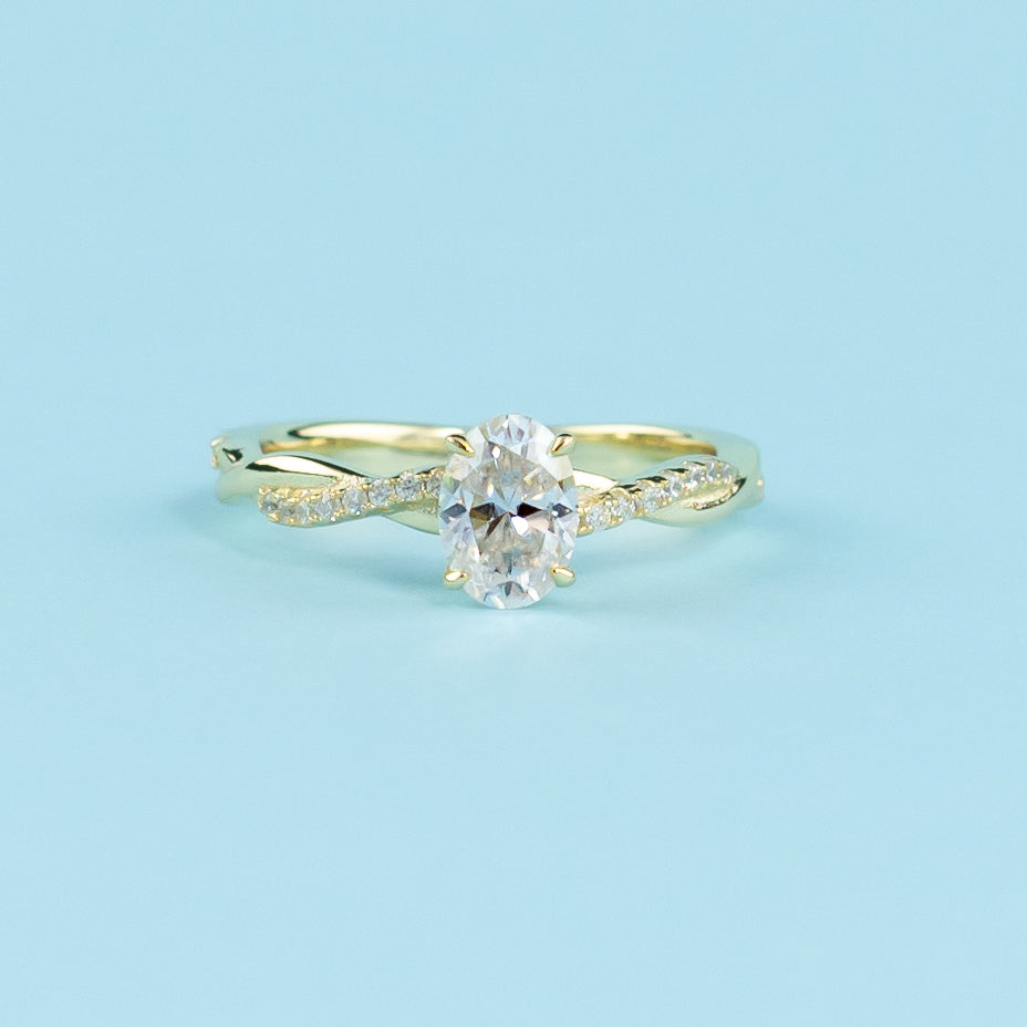 This ring showcases a beautiful oval moissanite set within a warm yellow gold band with a symbolic infinity twist.