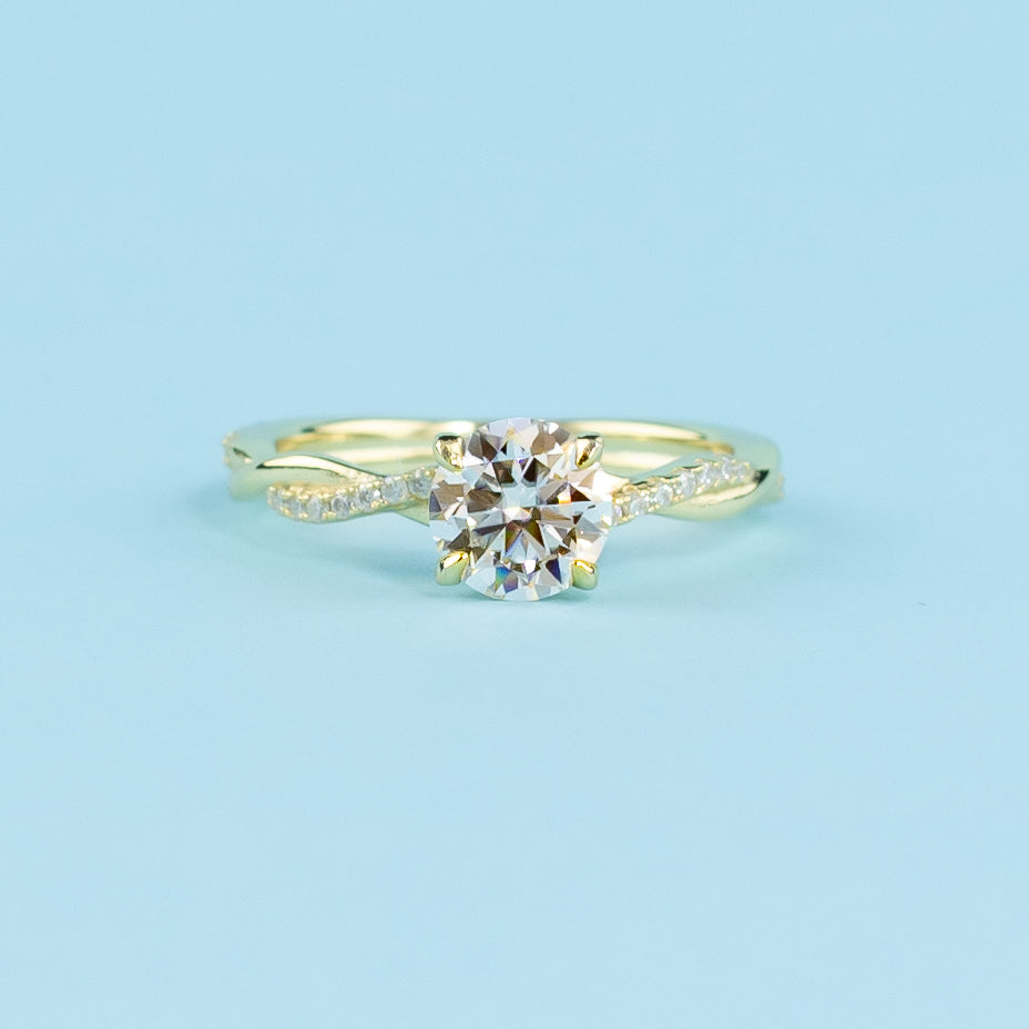 Showcases a brilliant round moissanite set in a warm yellow gold band with a symbolic infinity twist.