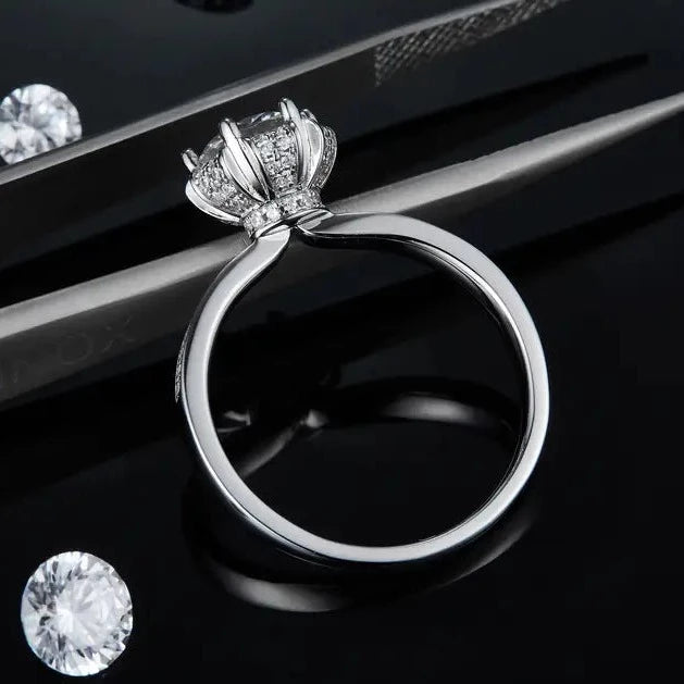 This ring features a 1.00ct moissanite surrounded by pave-set stones, with a vintage design and a polished sterling silver band.