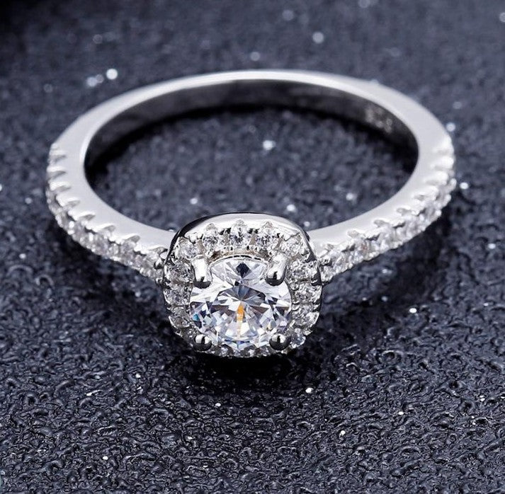 This elegant ring showcases a 0.50ct moissanite with a classic halo setting, crafted in polished sterling silver.