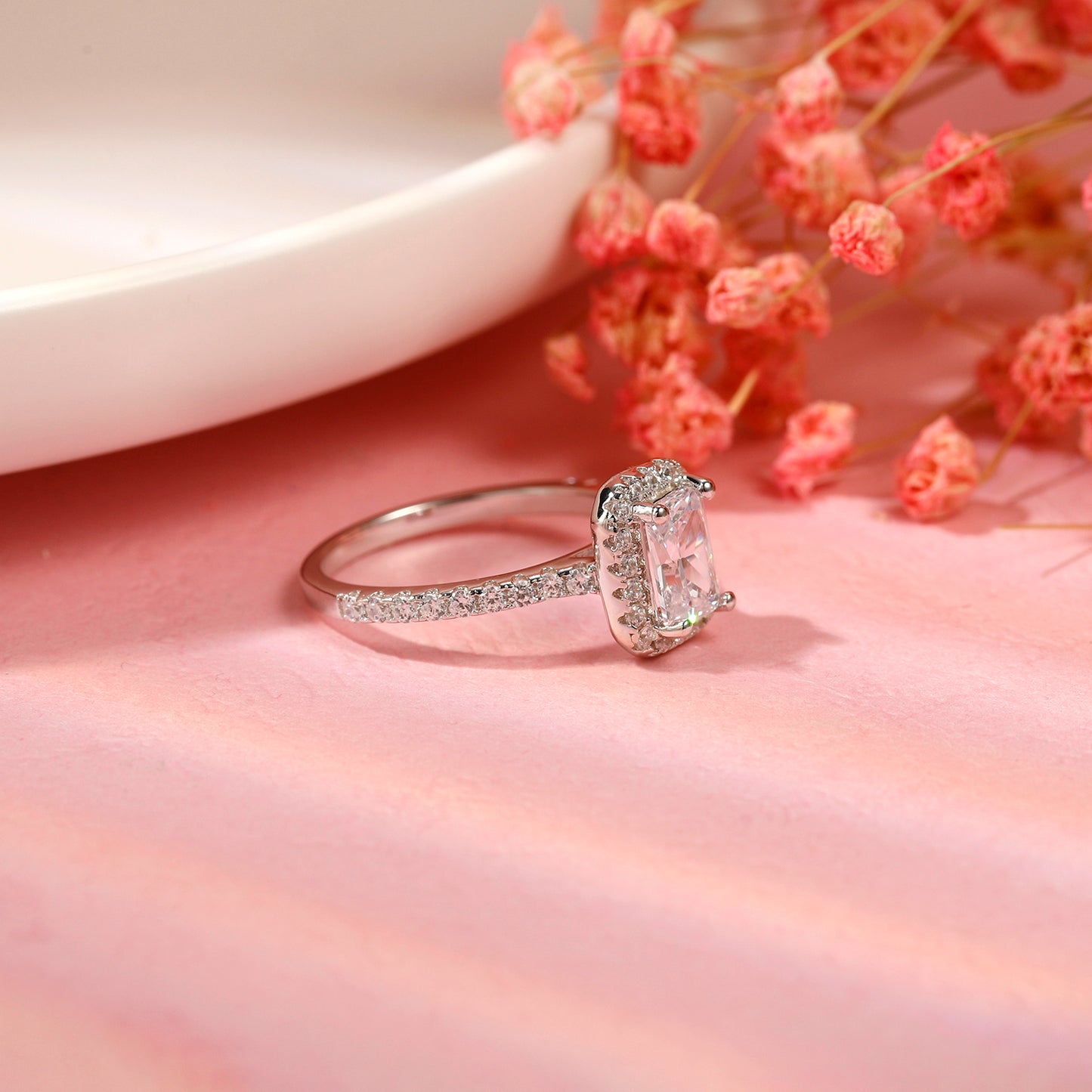 A stunning engagement ring featuring a 1.00ct emerald cut moissanite embraced by a halo of shimmering stones, set in a sleek sterling silver band.