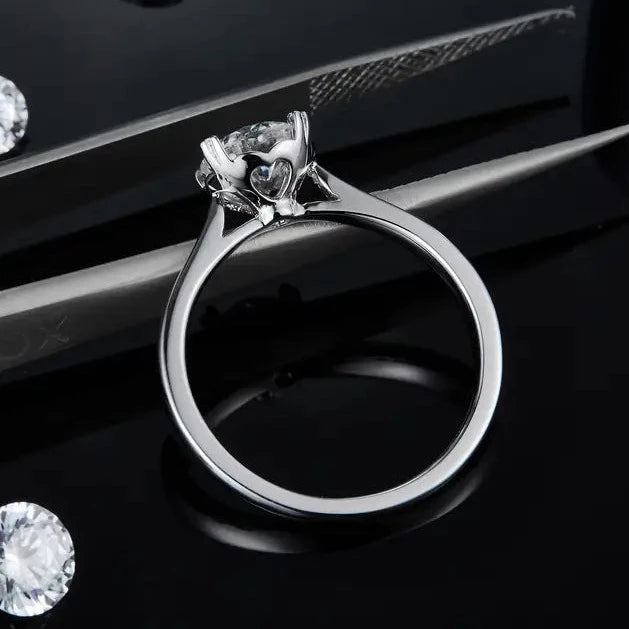This elegant ring features a 1.00ct moissanite held securely in a classic 4-prong setting with delicate heart-shaped claws.