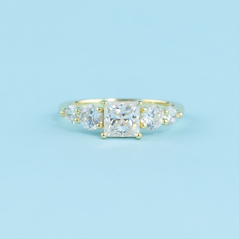 This elegant ring showcases five brilliant princess cut moissanites, representing love and commitment.