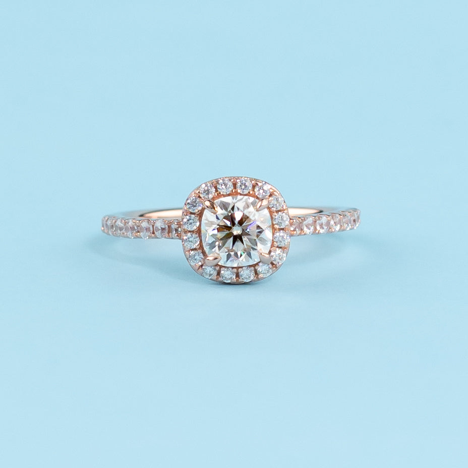 Elegant cushion cut moissanite engagement ring with a classic halo setting in warm 9ct rose gold.
