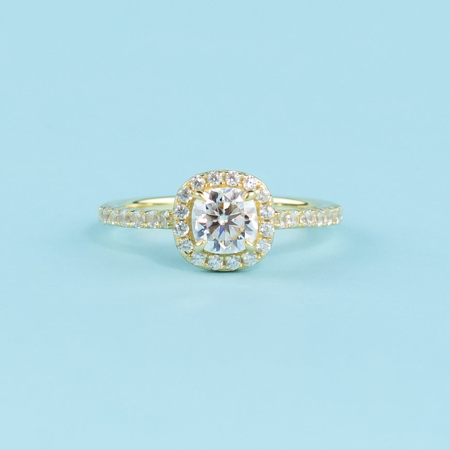 This ring showcases a brilliant cushion cut moissanite with a timeless halo setting in warm yellow gold.