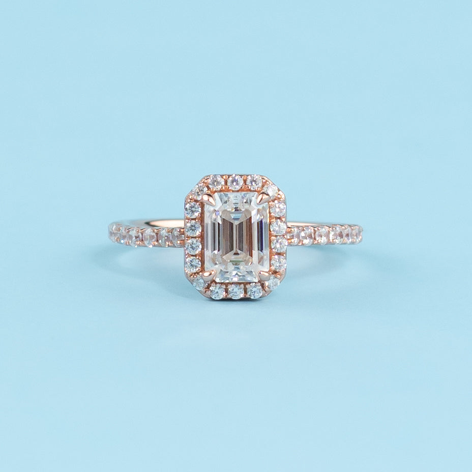 Elegant emerald cut moissanite engagement ring with a classic halo setting, crafted in warm 9ct rose gold.