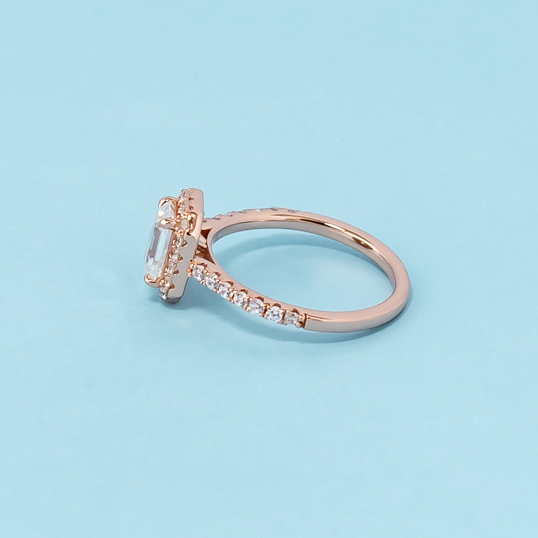 Stunning rose gold engagement ring featuring a sparkling emerald cut moissanite surrounded by a dazzling halo.
