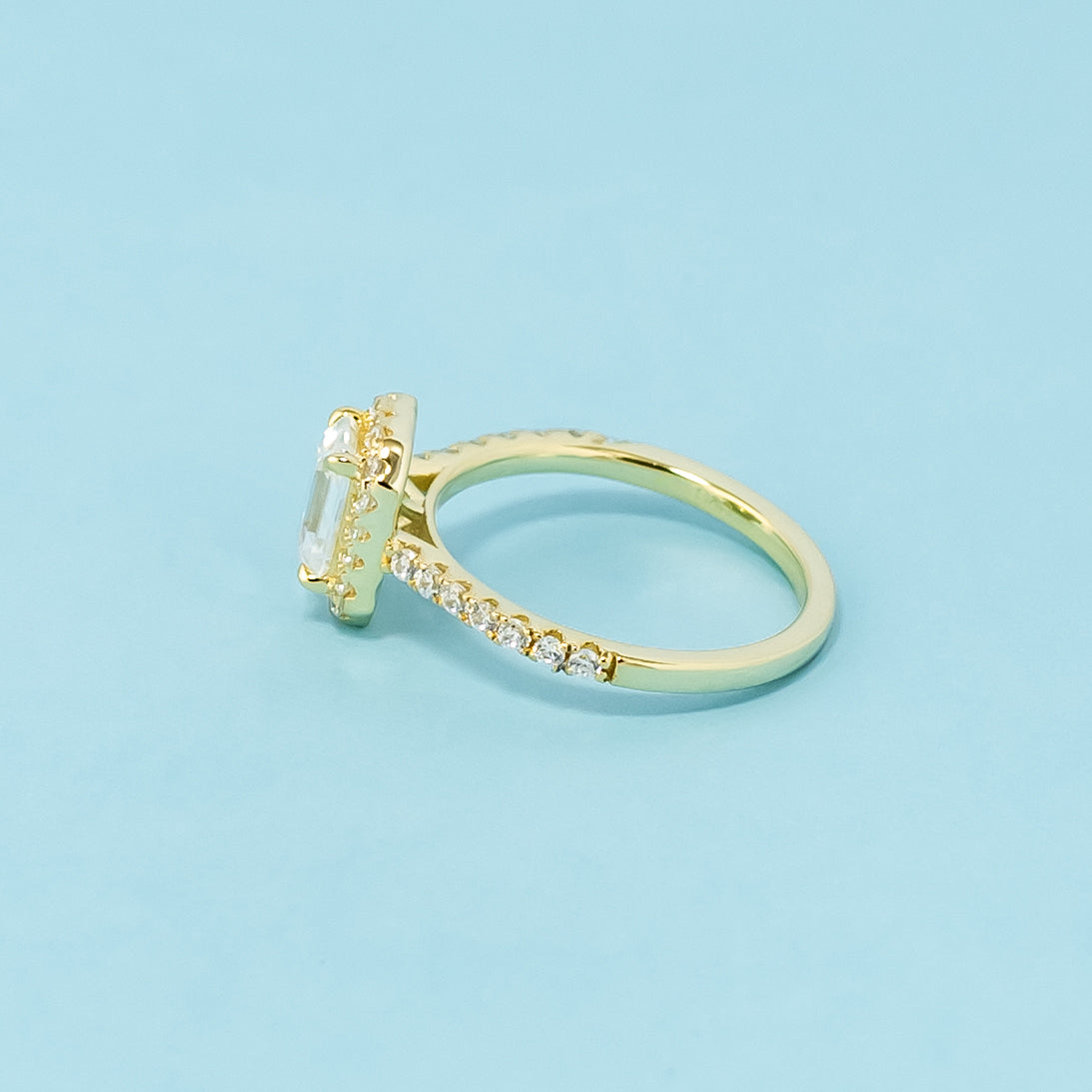 A beautiful halo design accentuates the elegance of an emerald cut moissanite in this 9ct yellow gold ring.