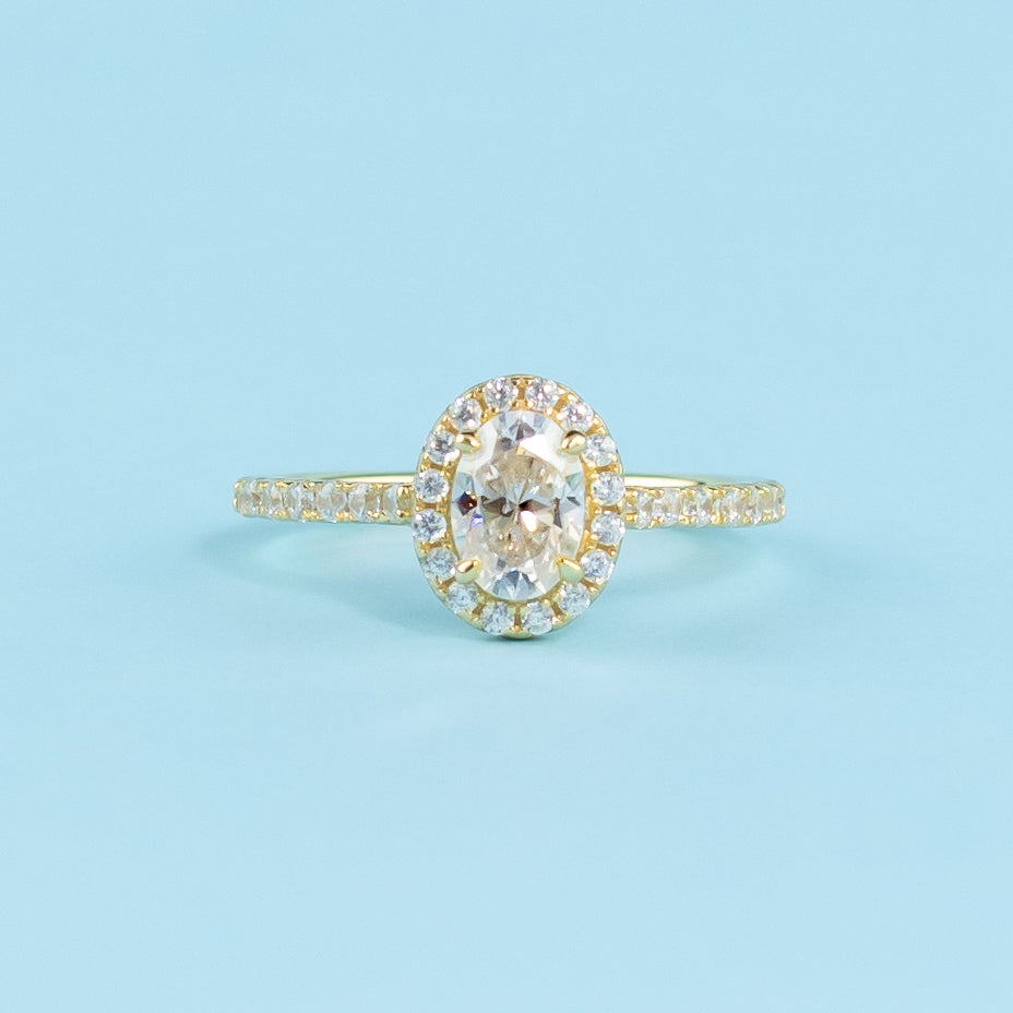 This ring showcases a brilliant oval cut moissanite with a timeless halo setting in warm yellow gold.