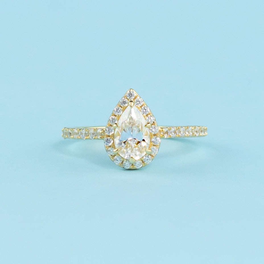 This ring showcases a brilliant pear-shaped moissanite with a timeless halo setting in warm yellow gold.