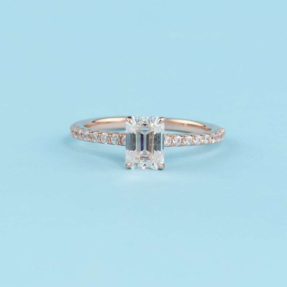 Elegant emerald cut moissanite engagement ring with a hidden halo setting in warm 9ct rose gold.