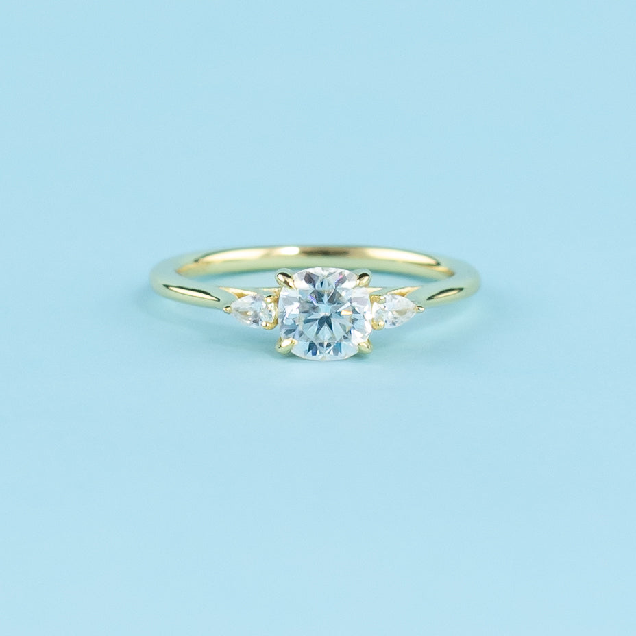 Showcases three sparkling cushion cut moissanites set in a warm 9ct yellow gold band, symbolizing eternal love.