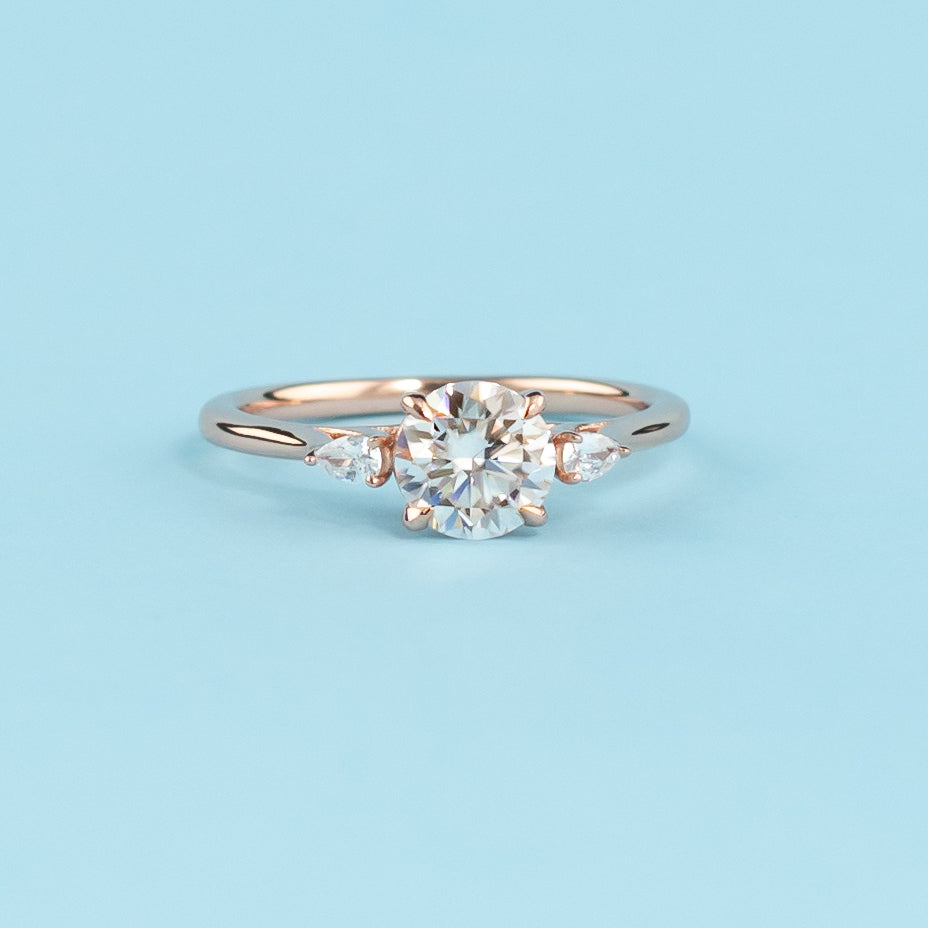 Stunning trilogy engagement ring with round brilliant moissanites, set in warm 9ct rose gold, symbolizing infinite love.