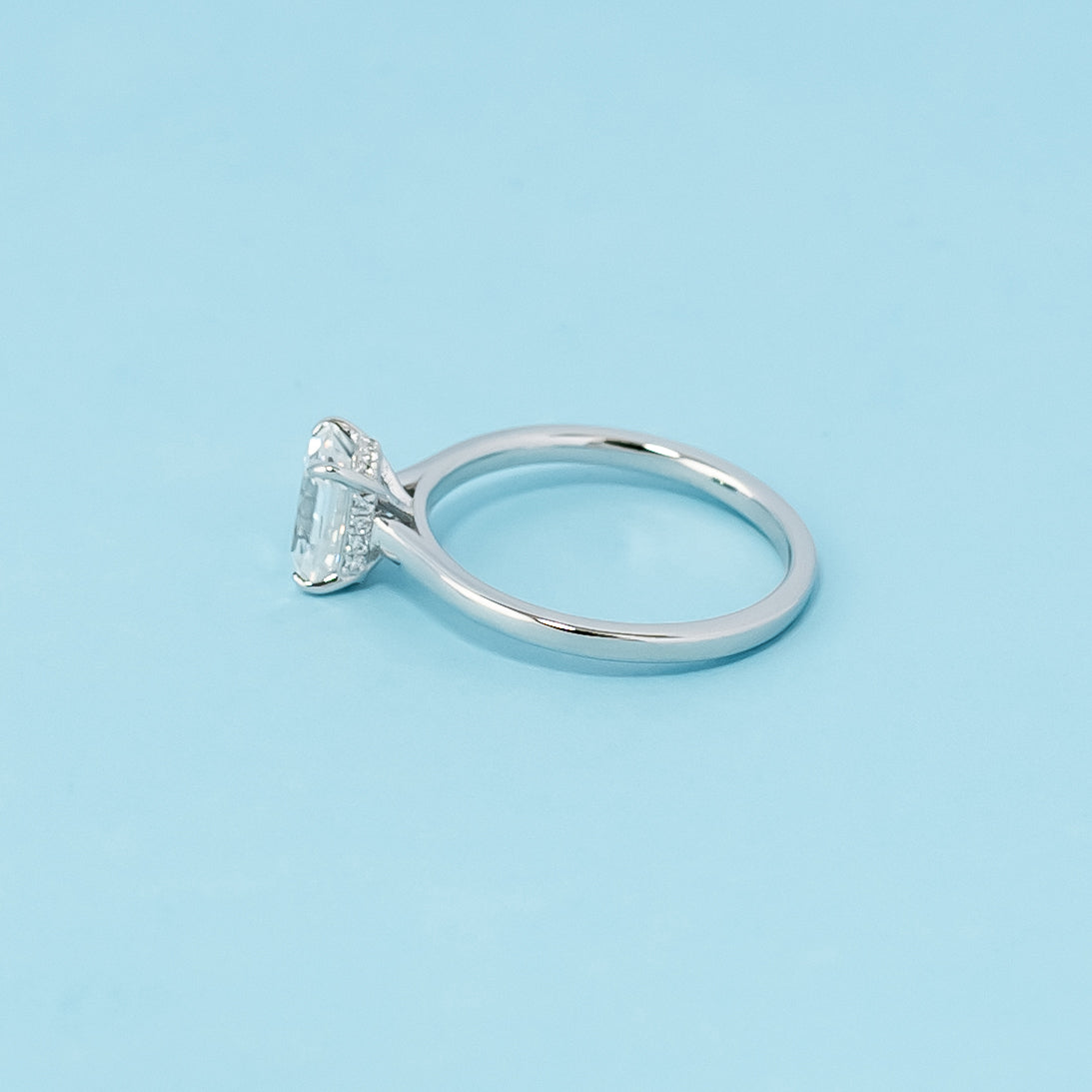 Modern and sophisticated engagement ring showcasing an emerald cut moissanite in a unique hidden halo design, crafted in 9ct white gold.