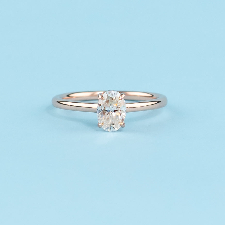 Elegant oval cut moissanite engagement ring with a delicate hidden halo, set in warm 9ct rose gold.
