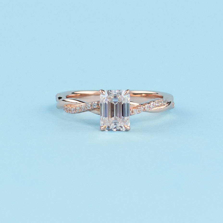 Elegant infinity engagement ring with an emerald cut moissanite, set in warm 9ct rose gold.
