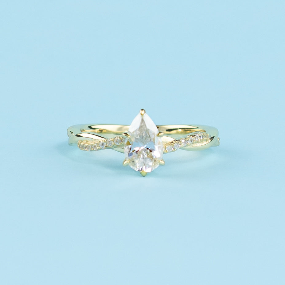 Showcases a beautiful pear-shaped moissanite set in a warm yellow gold band with a symbolic infinity twist.