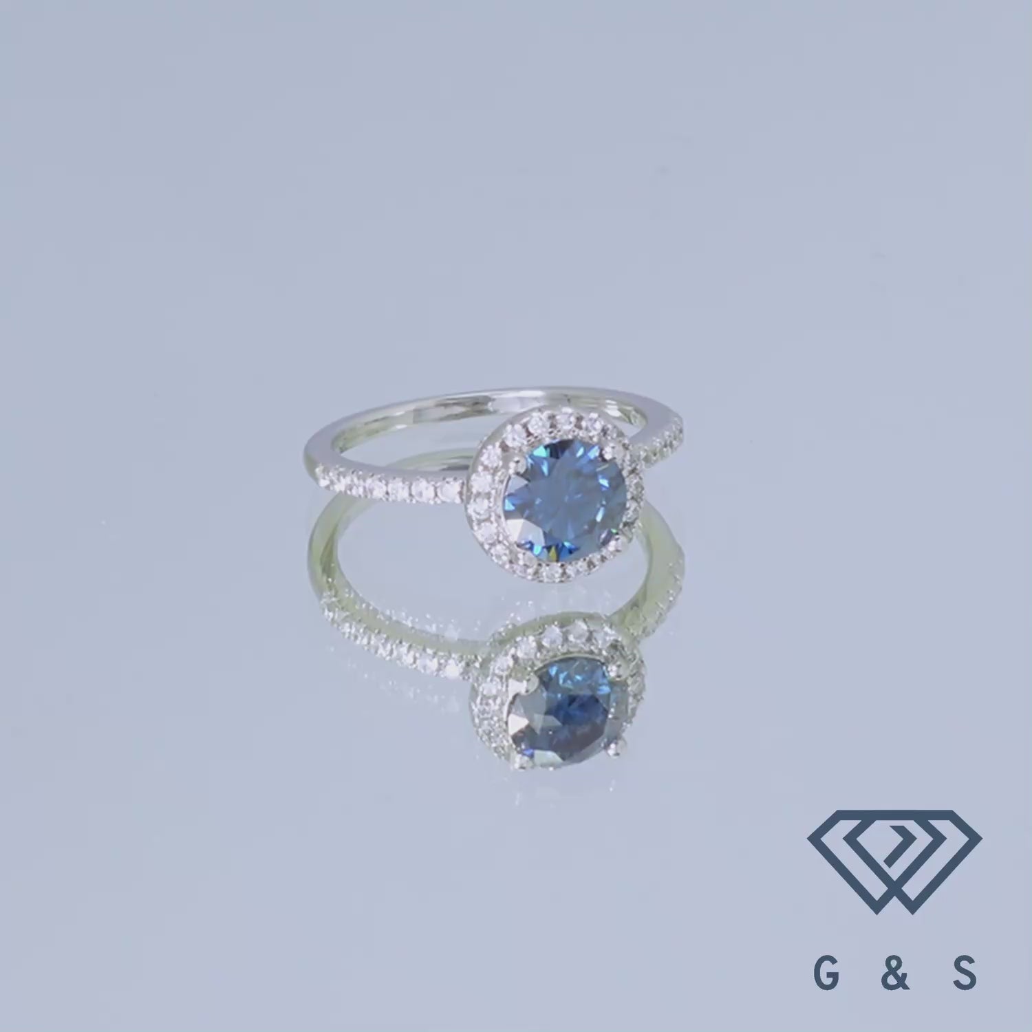 This ring features a brilliant blue moissanite center stone surrounded by a halo of smaller stones, enhancing its unique color and sparkle
