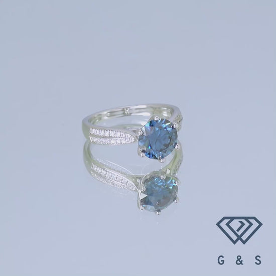 This elegant sterling silver ring showcases a dazzling 2.00ct blue moissanite center stone, enhanced by a sparkling pave band for a touch of classic glamour.