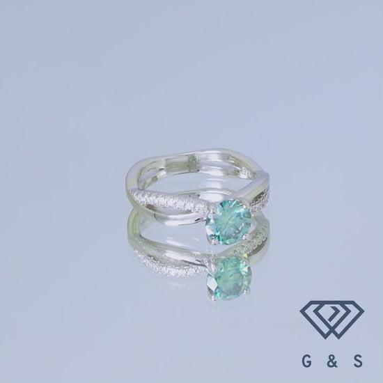 A close-up view of a 1.00ct green moissanite set within a polished sterling silver infinity design, showcasing the stone's unique color and the ring's intricate details.